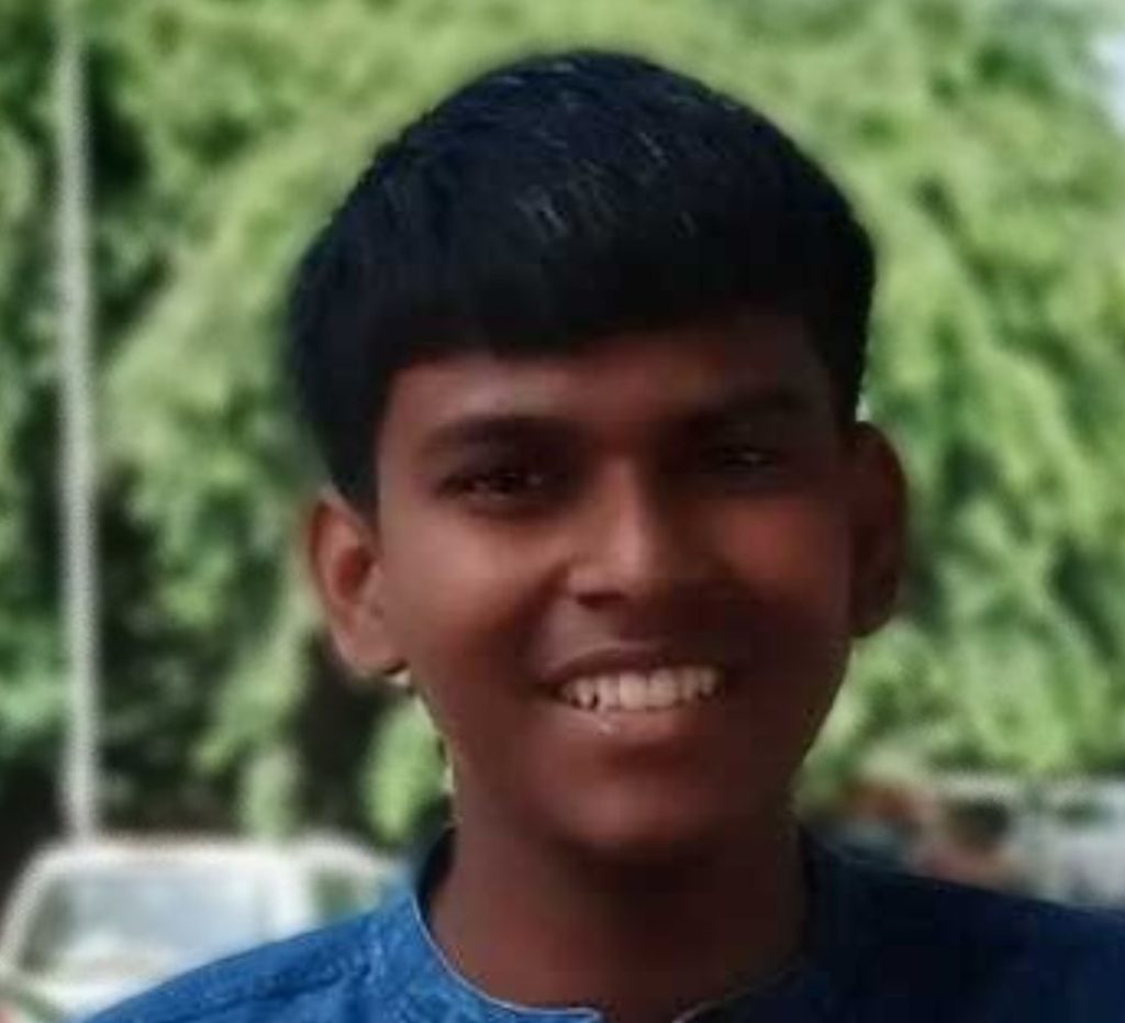 Headshot of Ashutosh. He is smiling towards the camera and there are trees and cars in the background